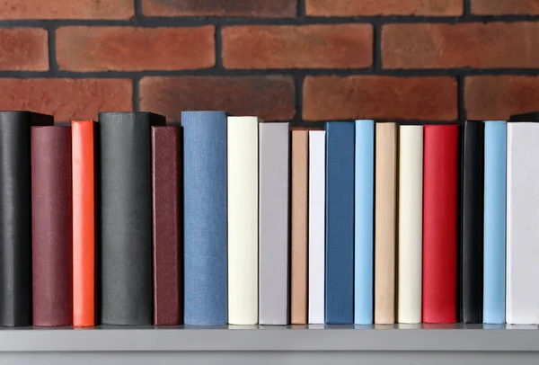 Many different hardcover books on grey table near brick wall