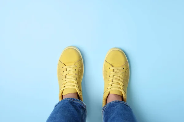 Woman in stylish sneakers on light blue background, top view