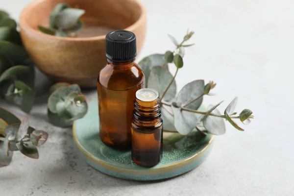 Flaschen Mit Ätherischem Eukalyptusöl Und Pflanzenzweigen Auf Hellgrauem Tisch — Stockfoto