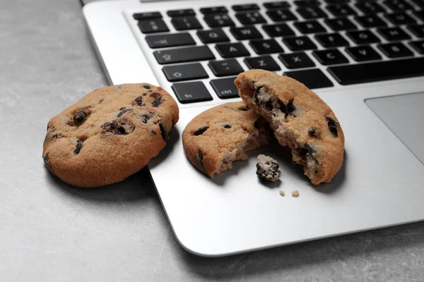 Chocolate chip cookies and laptop on light grey table, closeup