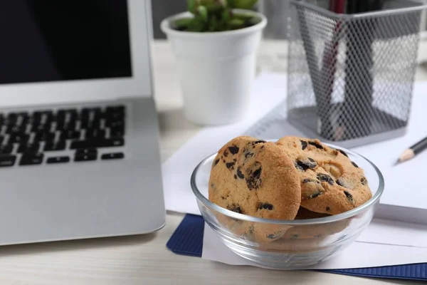 Bowl with chocolate chip cookies on white wooden table in office. Space for text