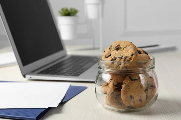 Jar with chocolate chip cookies on white wooden table in office, closeup. Space for text