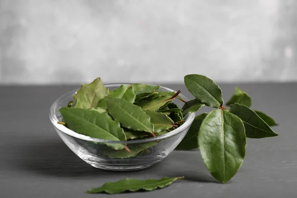 Fresh green bay leaves in bowl on gray wooden table