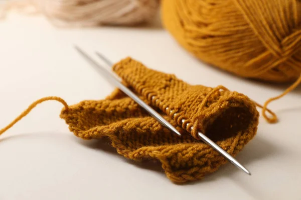 Soft orange knitting and metal needles on beige background, closeup
