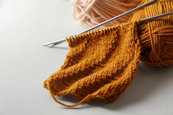 Soft orange knitting, colorful yarns and metal needles on beige background, closeup