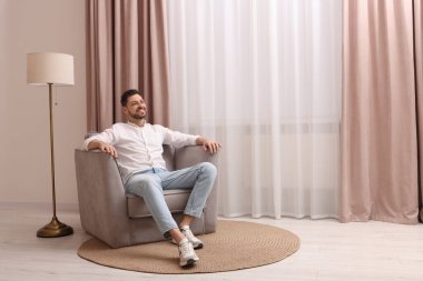 Evdeki güzel perdelerle pencerenin yanındaki koltukta dinlenen mutlu adam. Metin için boşluk