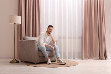 Evdeki güzel perdelerle pencerenin yanındaki koltukta dinlenen mutlu adam. Metin için boşluk