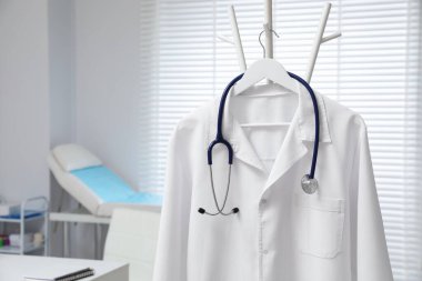 Klinikte askıda asılı duran beyaz doktor önlüğü ve steteskop, yakın plan. Metin için boşluk