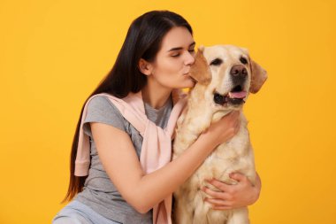 Mutlu kadın turuncu arka planda şirin Labrador Retriever 'ı öpüyor