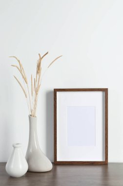 Boş fotoğraf çerçevesi ve vazo. Ahşap masa üzerinde kuru dekoratif çiviler. Tasarım için model