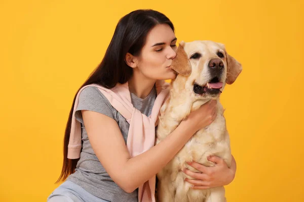 快乐的女人在橙色背景下亲吻可爱的拉布拉多猎犬 — 图库照片