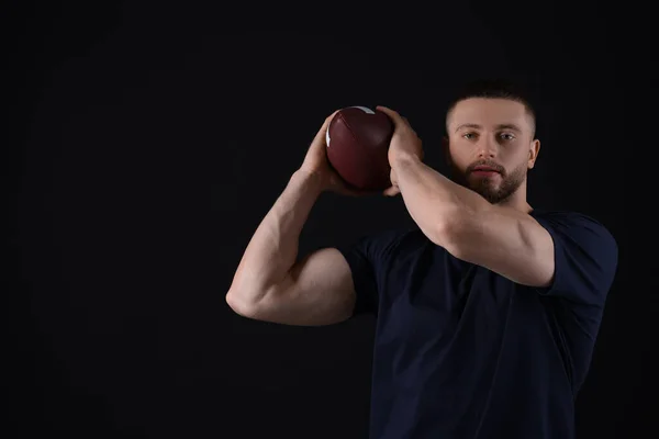 stock image Athletic young man with American football ball on black background. Space for text