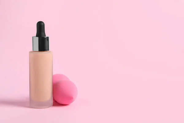 Bottle of skin foundation and sponge on pink background, space for text. Makeup product