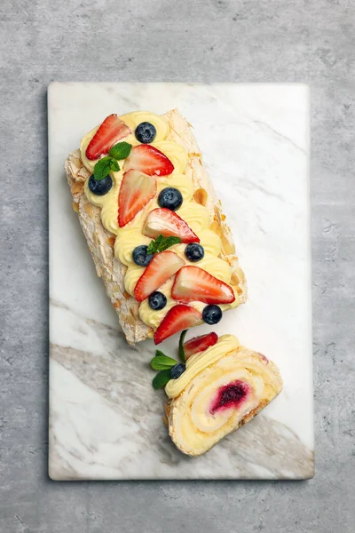Tasty meringue roll with jam, cream, strawberry, blueberry and mint on light grey table, top view