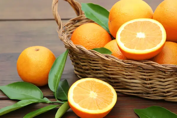 Weidenkorb Reife Saftige Orangen Und Grüne Blätter Auf Holztisch Nahaufnahme — Stockfoto
