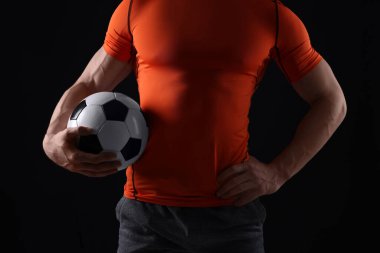 Siyah arka planda futbol topu olan atletik adam, yakın plan.