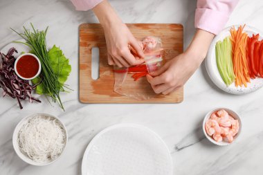 Lezzetli börek yapıyorum. Beyaz mermer masada taze sebze ve karidesleri pirinç kağıdına saran kadın.