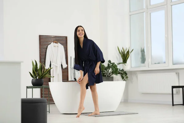 stock image Beautiful happy woman wearing stylish bathrobe near tub in bathroom