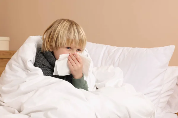 男孩在家里的床上用鼻涕在组织里吹气 感冒症状 — 图库照片