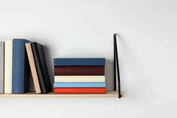Wooden shelf with many hardcover books on white wall