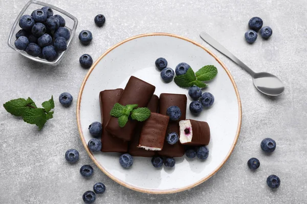 Delicious glazed curd snacks with fresh blueberries and mint on light grey table, flat lay