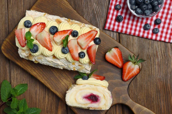 Tasty meringue roll with jam, cream, strawberry, blueberry and mint on wooden table, flat lay