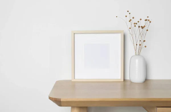 Empty photo frame and vase with dry decorative flowers on wooden table. Mockup for design