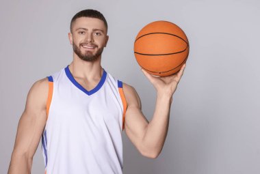 Açık gri arka planda basketbol topu olan atletik genç bir adam. Metin için boşluk