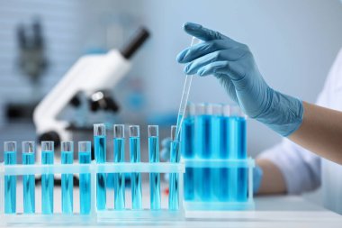 Bilim adamı laboratuarda test tüpünden damlatıcıyla numune alıyor.