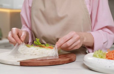 Lezzetli börek yapıyorum. Beyaz masada malzemeleri pirinç kağıdına saran kadın, yakın plan.