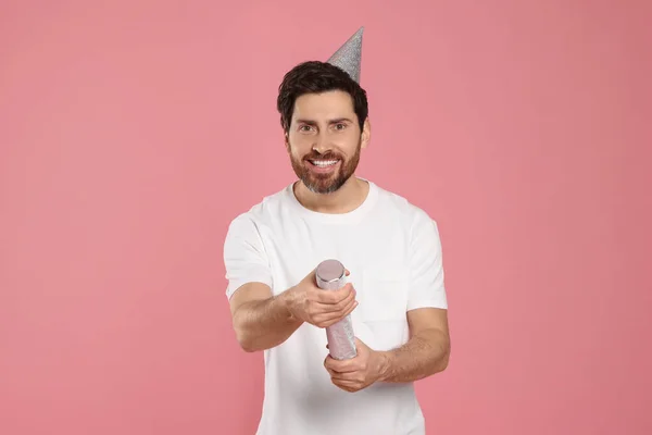 Happy man with party popper on pink background