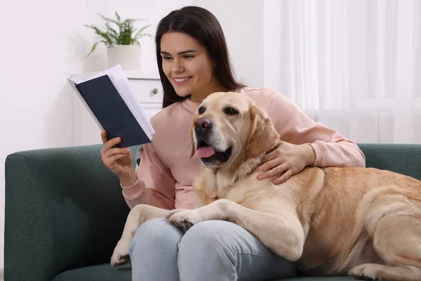 快乐的女人和可爱的拉布拉多猎犬坐在沙发上看书 — 图库照片