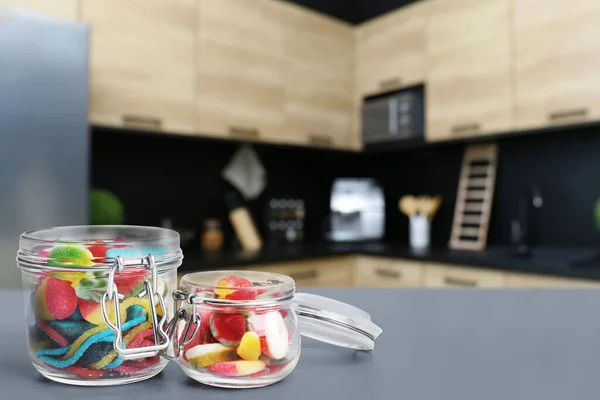 Glass jars with tasty gummy candies on grey table in kitchen. Space for text