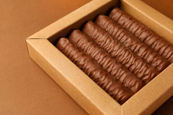 Sweet tasty chocolate bars in box on brown background, closeup