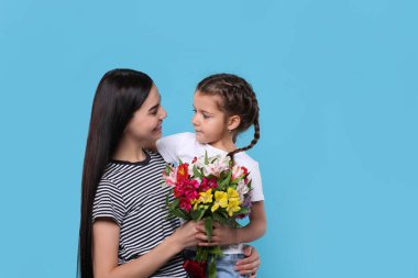 Kızıyla mutlu bir kadın ve açık mavi arka planda bir buket güzel çiçek, mesaj için yer. Anneler günü kutlaması.
