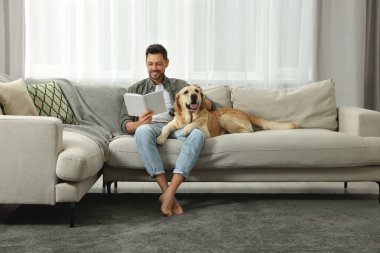 Evdeki şirin Labrador Retriever 'ının yanındaki kanepede kitap okuyan adam. Metin için boşluk