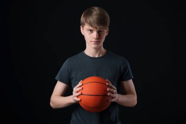 Siyah arka planda basketbol topu olan genç bir çocuk.