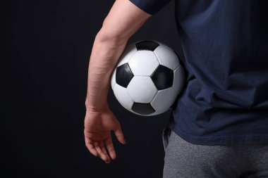 Siyah arka planda futbol topu olan atletik adam, yakın plan.