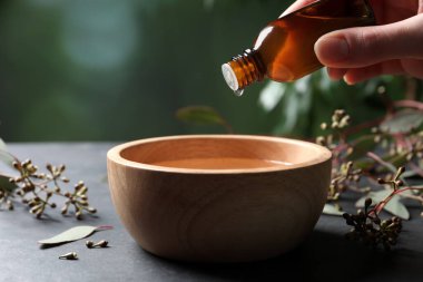 Kadın okaliptüs yağı damlatıyor şişeden kaseye, yakın plan gri masada.