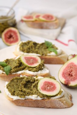 Krem peynirli lezzetli bruschettalar, pesto sosu, incir ve taze fesleğen, yakın plan.