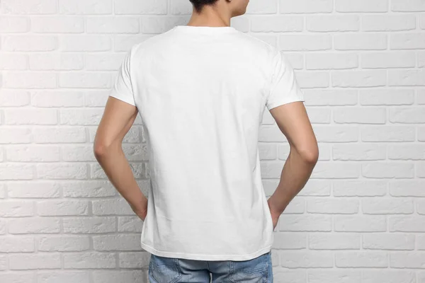 Man wearing stylish t-shirt near white brick wall, back view. Mockup for design