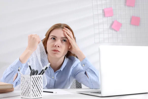 一个愤怒的女人在办公室的桌子前卷起了泡沫 缓解压力 — 图库照片