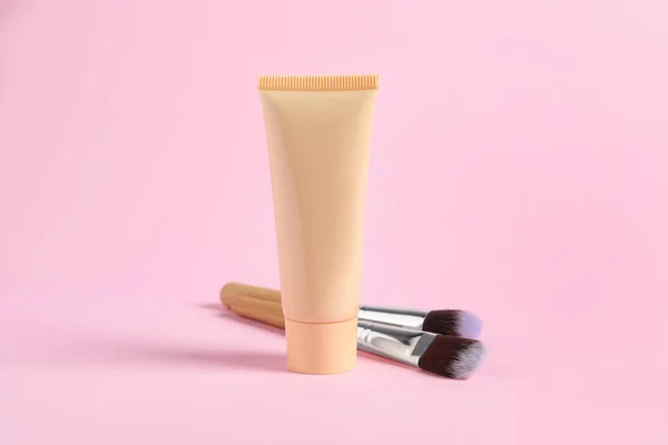 Tube of skin foundation and brushes on pink background. Makeup product
