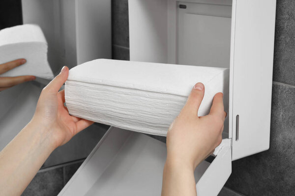 Woman putting new fresh paper towels into dispenser in bathroom, closeup