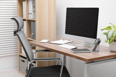 Cozy workspace with computer on desk, chair and bookcase near white wall at home