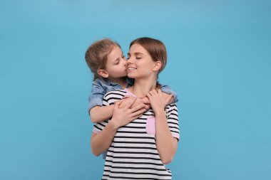 Küçük kız annesini açık mavi arka planda öpüyor. Anneler Günün kutlu olsun.