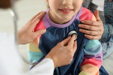 Anne ve kızının doktorla randevusu var. Pediyatrist steteskopla hastayı muayene ediyor.