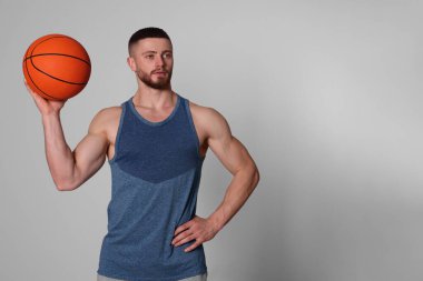 Açık gri arka planda basketbol topu olan atletik genç adam.
