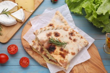 Peynirli, biberiyeli ve açık mavi ahşap masadaki farklı ürünlü lezzetli pizza calzone 'leri.