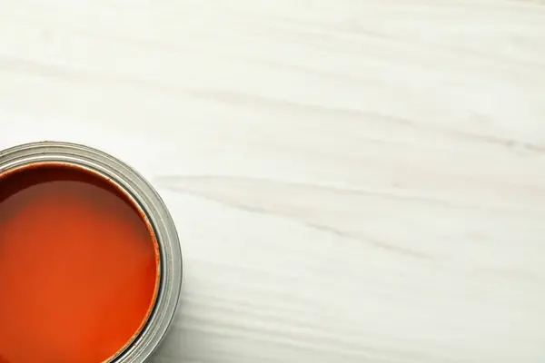 Can of orange paint on white wooden table, top view. Space for text